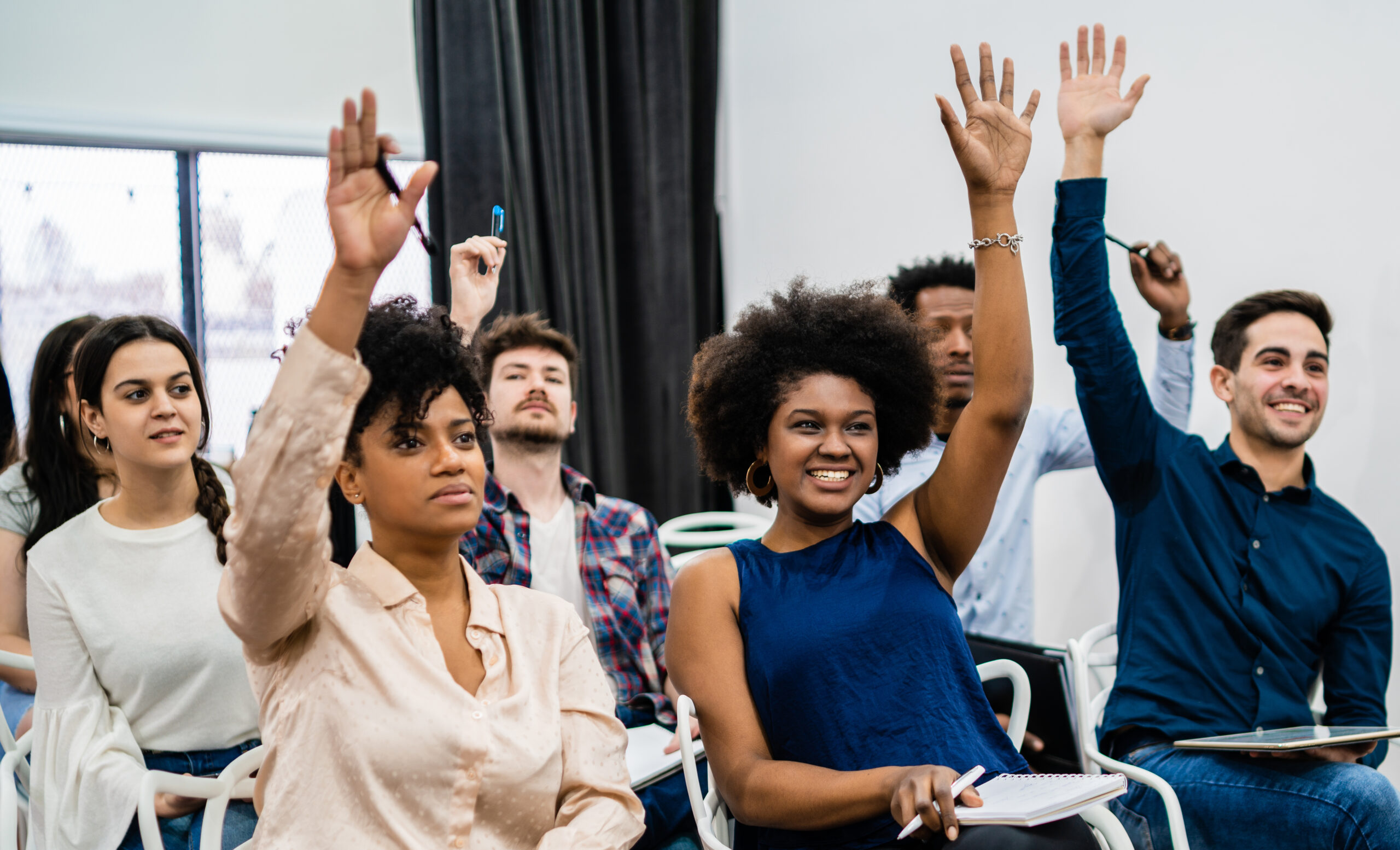 Group of young people sitting on conference together. Group of young people sitting on conference together while raising their hands to ask a question. Business team meeting seminar training concept.